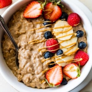 A bowl of protein oatmeal topped with fresh berries, banana slices, and a drizzle of nut butter.