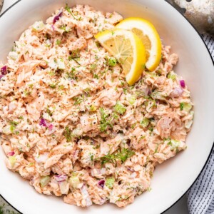 Salmon salad in a white bowl with two lemon slices.