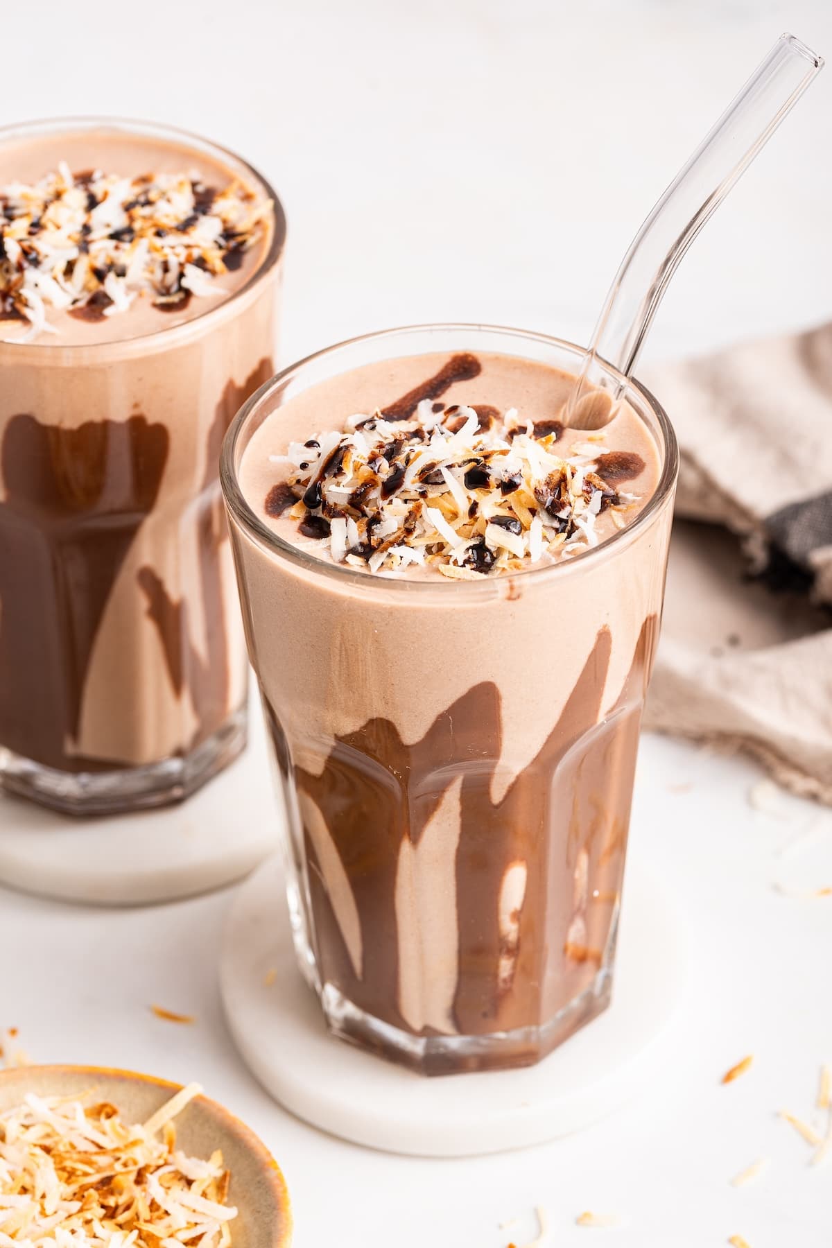 A samoa cookie protein shake in a glass topped with coconut and drizzled chocolate. The glass has drizzled chocolate around the sides.