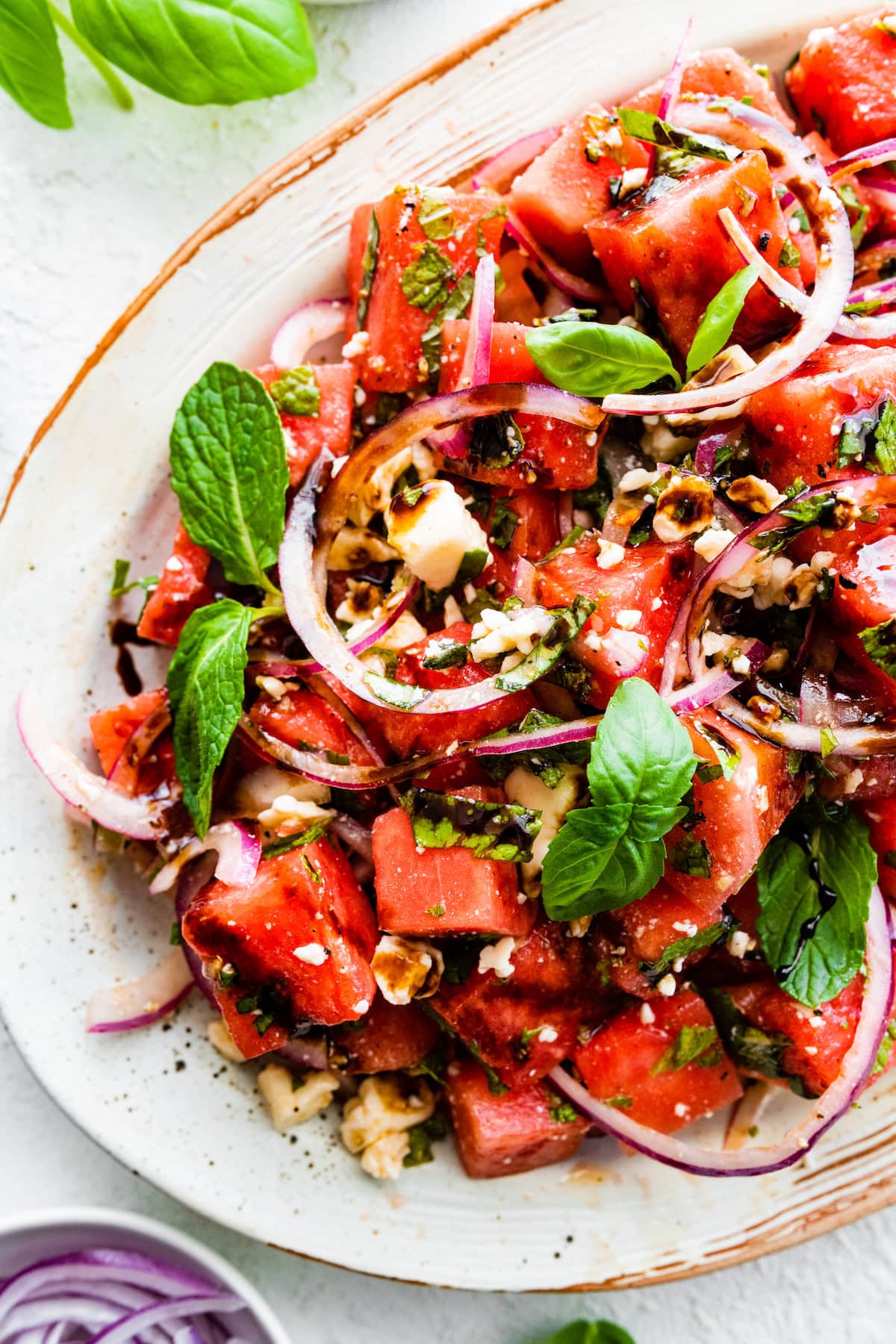 A watermelon salad with crumbled feta cheese, fresh basil, balsamic vinegar, and red onions.