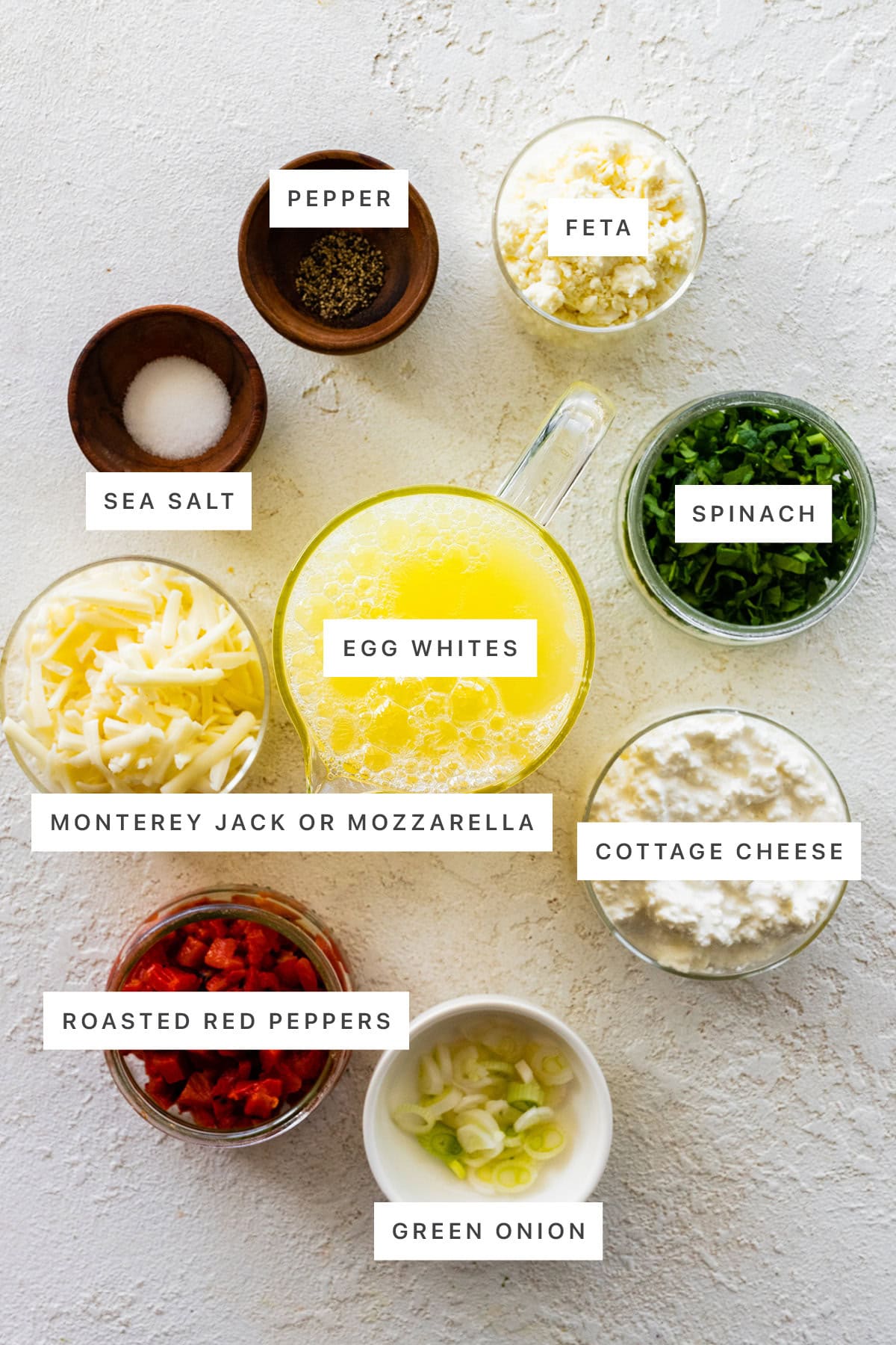 Ingredients measured out to make Egg White Bites: pepper, sea salt, feta, Monterey jack cheese, egg whites, spinach, roasted red peppers, cottage cheese and green onion.