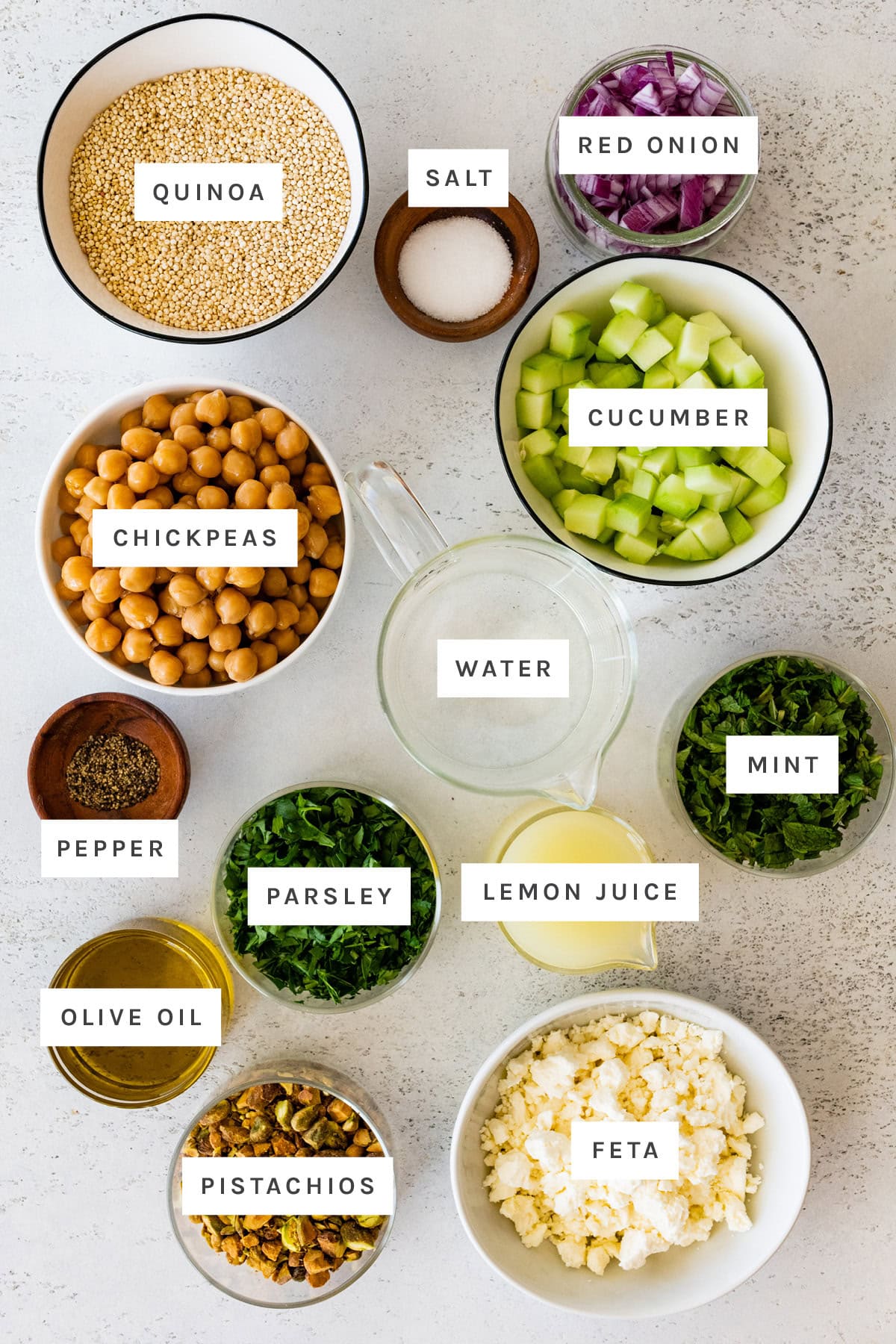 Ingredients measured out to make the Jennifer Aniston salad: salt, pepper, mint, quinoa, chickpeas, red onion, lemon juice, pistachios, feta, parsley, cucumber, water and olive oil.