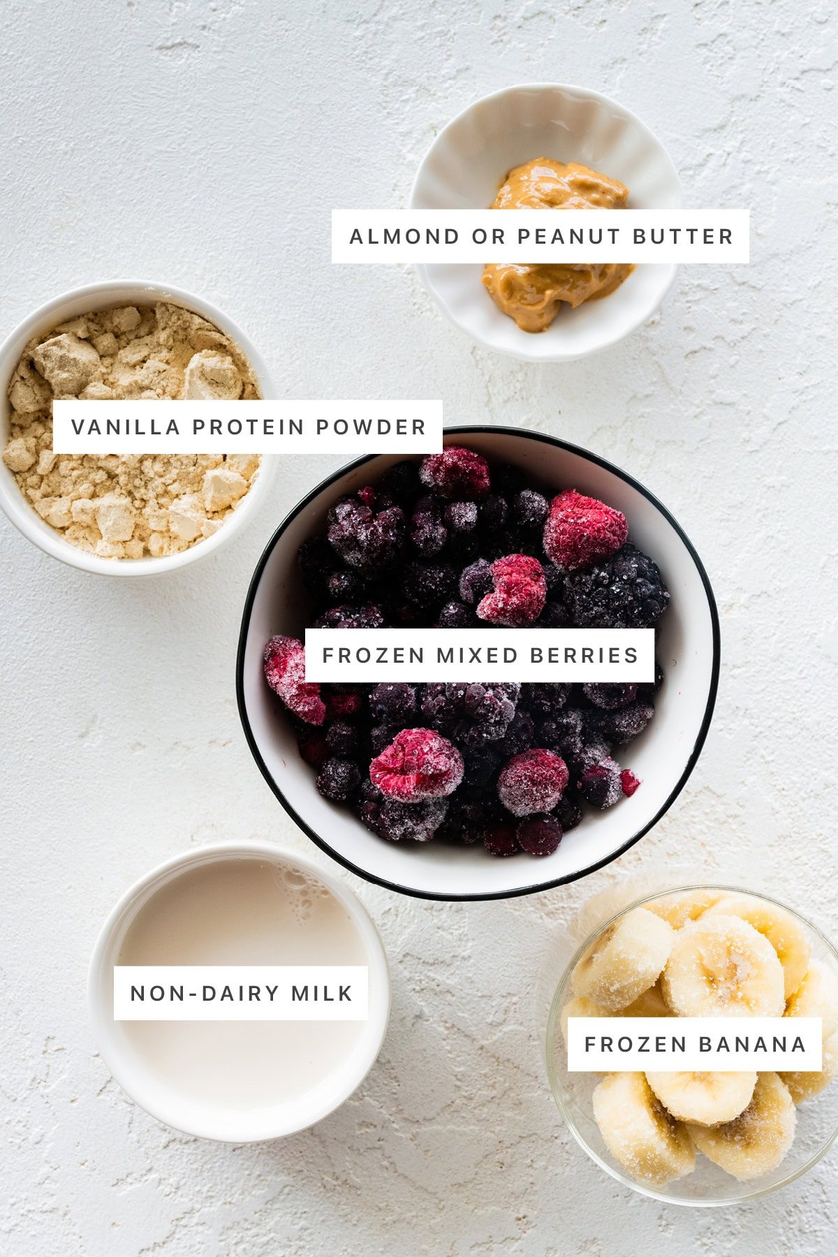 Ingredients measured out to make a Smoothie Bowl: vanilla protein powder, almond or peanut butter, frozen mixed berries, non-dairy milk and frozen banana.