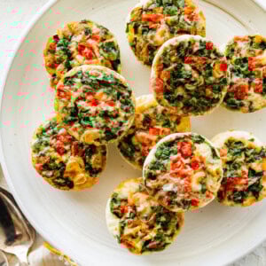 Multiple egg white bites topped with cheese and veggies rest on a white plate.