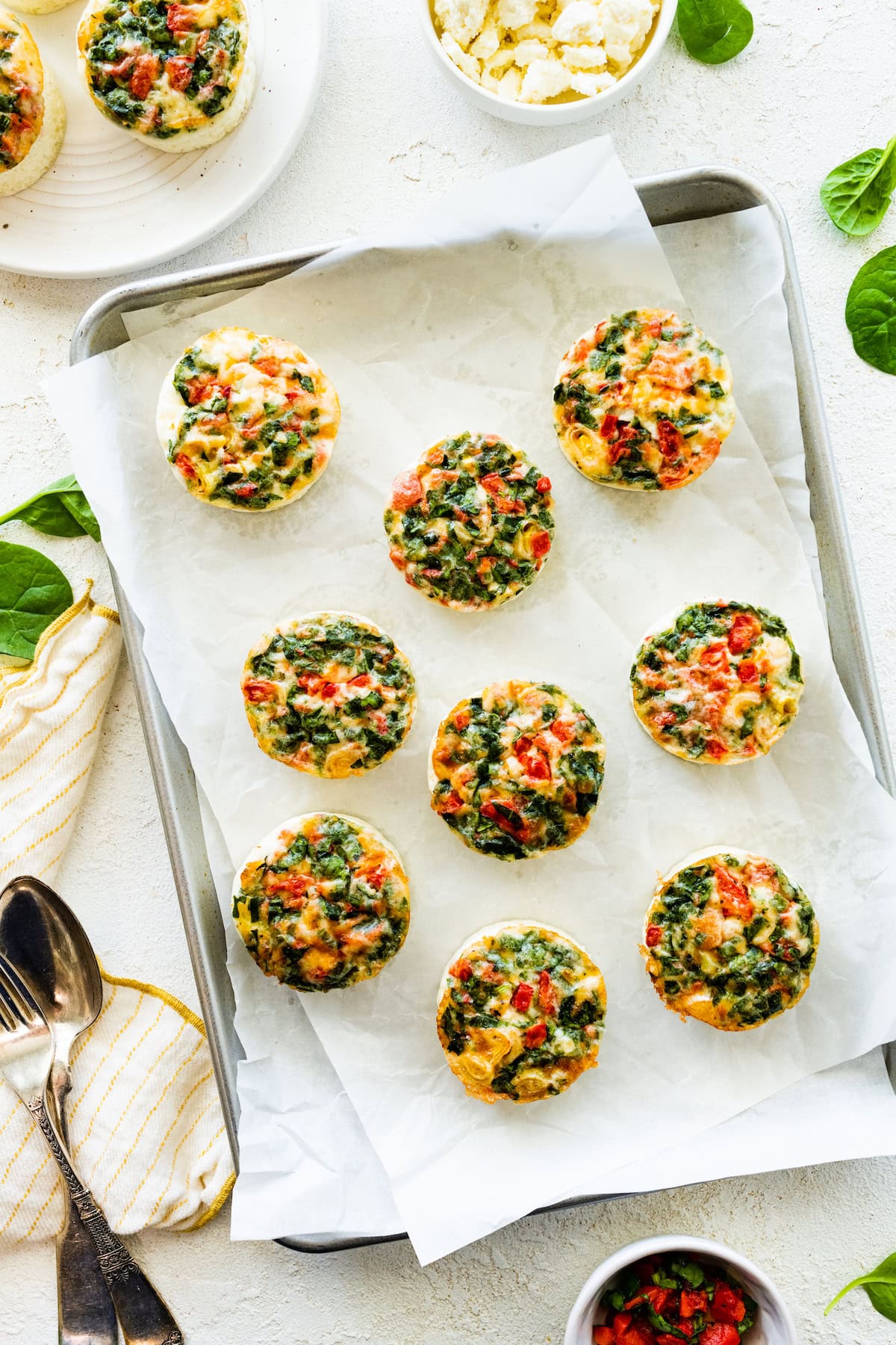 Multiple egg white bites topped with cheese and veggies sit on a baking tray.