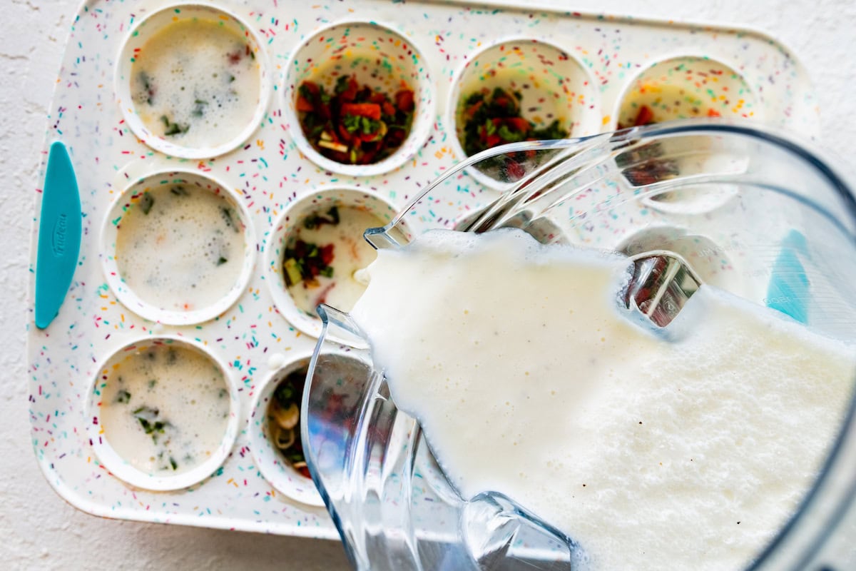 An egg white mixture in a glass bowl is poured into a muffin pan.