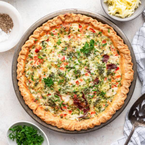 An unsliced cooked egg white quiche in a metal pie dish. Quiche is topped with fresh herbs.
