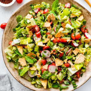 A large bowl of fattoush salad with ingredients like radishes, cherry tomatoes, lettuce, pita chips, and more.