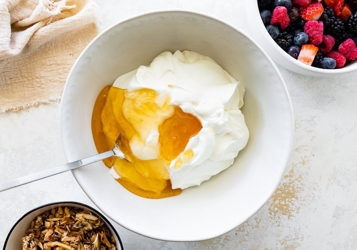 A large mixing bowl of yogurt and honey with a metal spoon.