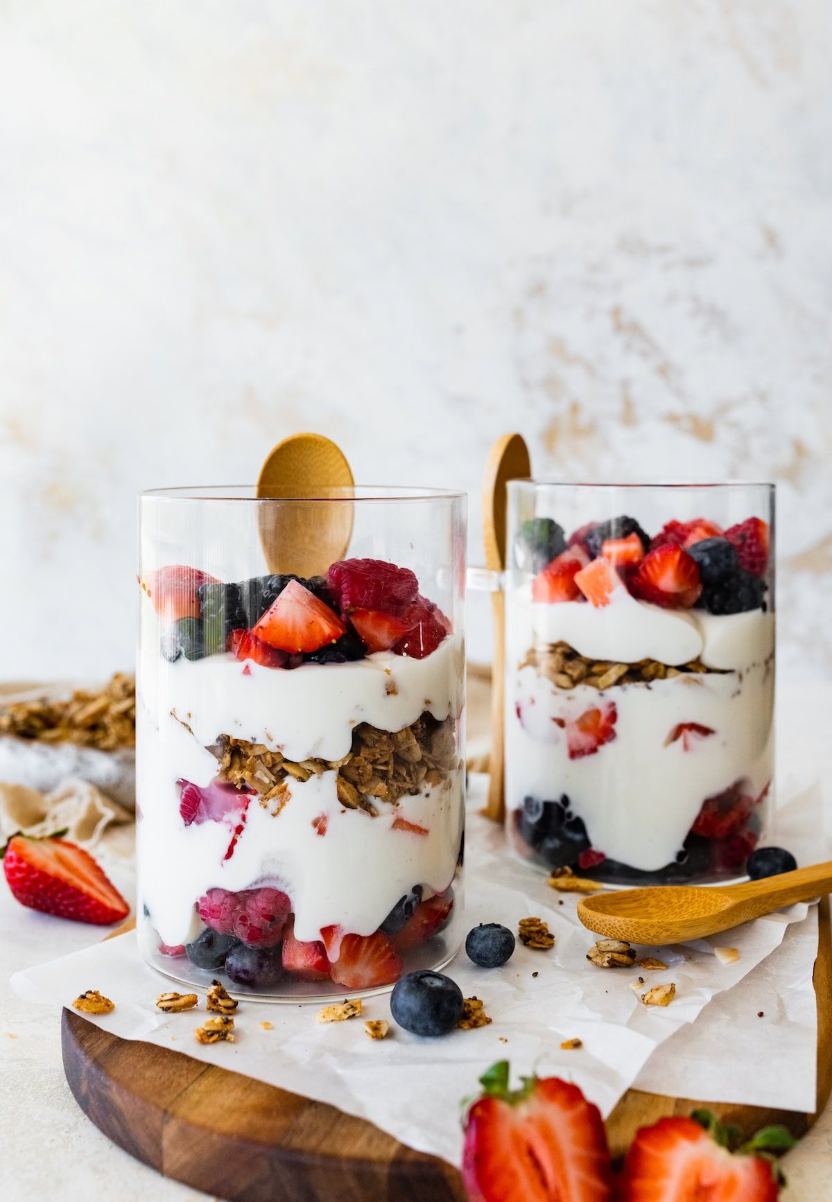 Two glass cups of fruit and yogurt parfaits. The cups are layered with fruit, yogurt, granola, then yogurt again and more fruit on top.