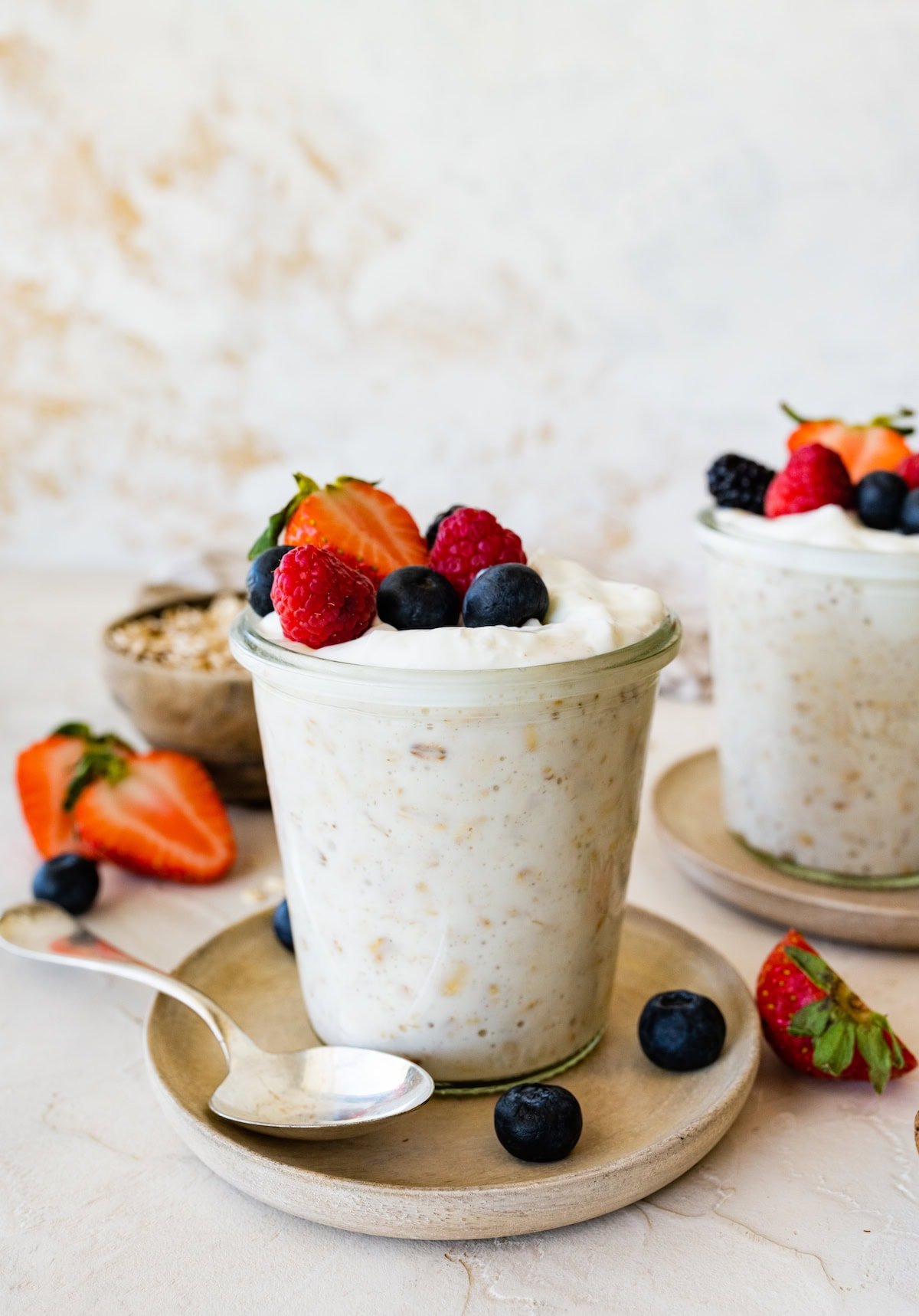 Overnight oats with yogurt in a glass cup, on a small plate, and topped with fresh berries.