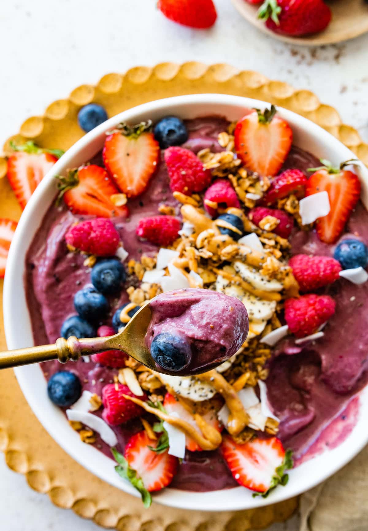 A spoon with a bite-size portion of a protein acai smoothie over a smoothie bowl.