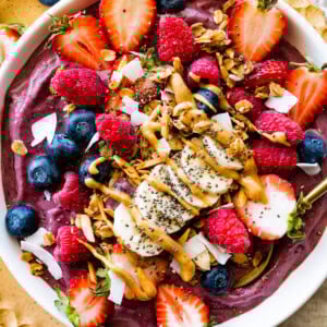 A protein acai bowl topped with fresh berries, banana slices, chia seeds, coconut shreds, and a drizzle of almond butter.