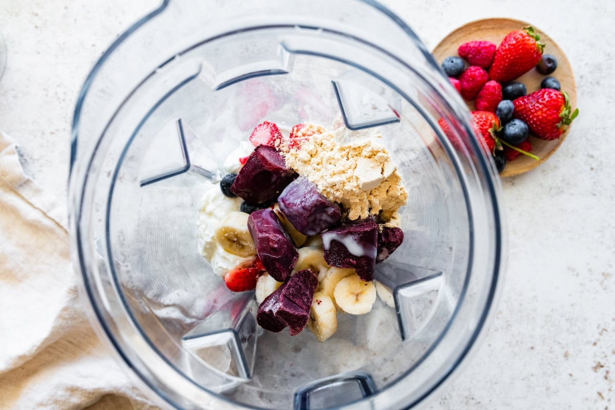 A blender full of frozen acai, banana slices, strawberries, and protein powder.