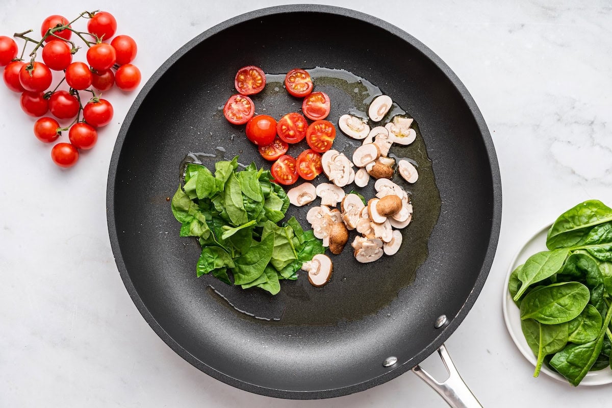 Mushrooms, spinach, and cherry tomatoes in a skillet.