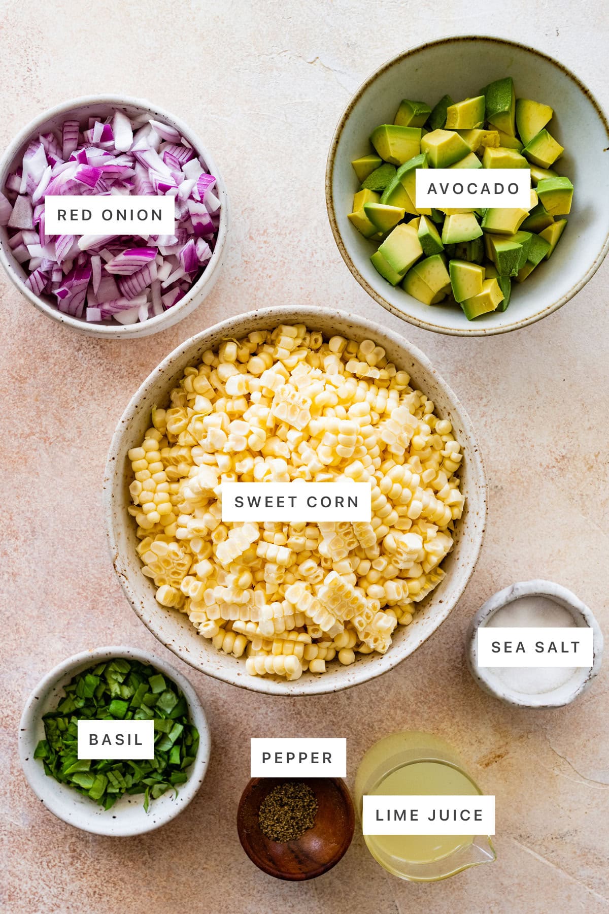 Ingredients measured out to make Avocado Corn Salad: red onion, avocado, sweet corn, basil, pepper, lime juice and sea salt.