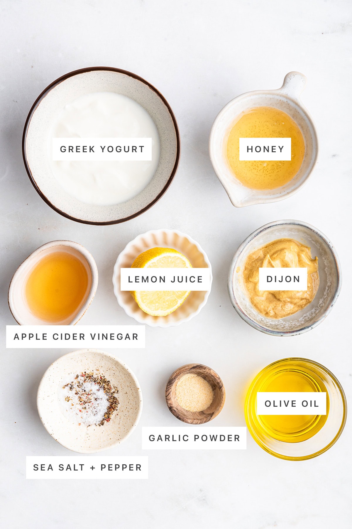 Ingredients measured out to make Creamy Honey Mustard Dressing: Greek yogurt, honey, apple cider vinegar, lemon juice, dijon, sea salt, pepper, garlic powder and olive oil.