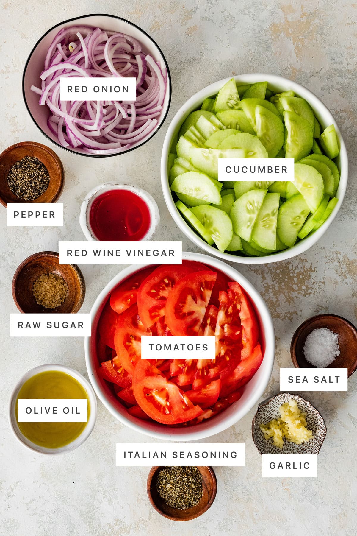 Ingredients measured out to make Cucumber Tomato Salad: red onion, cucumber, pepper, red wine vinegar, raw sugar, tomatoes, sea salt, olive oil, Italian seasoning and garlic.