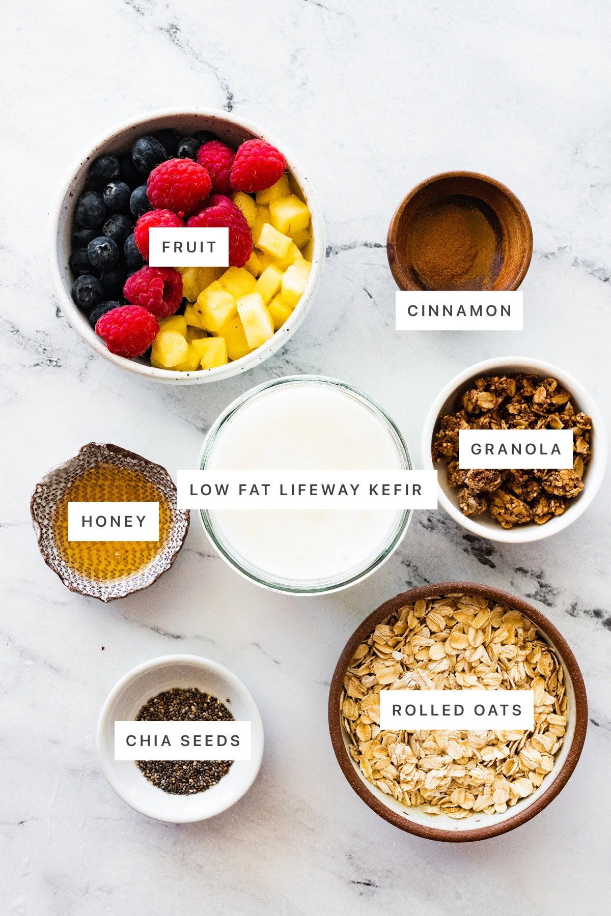 Ingredients measured out to make Kefir Overnight Oats: fruit, cinnamon, granola, low fat Lifeway kefir, honey, chia seeds and rolled oats.