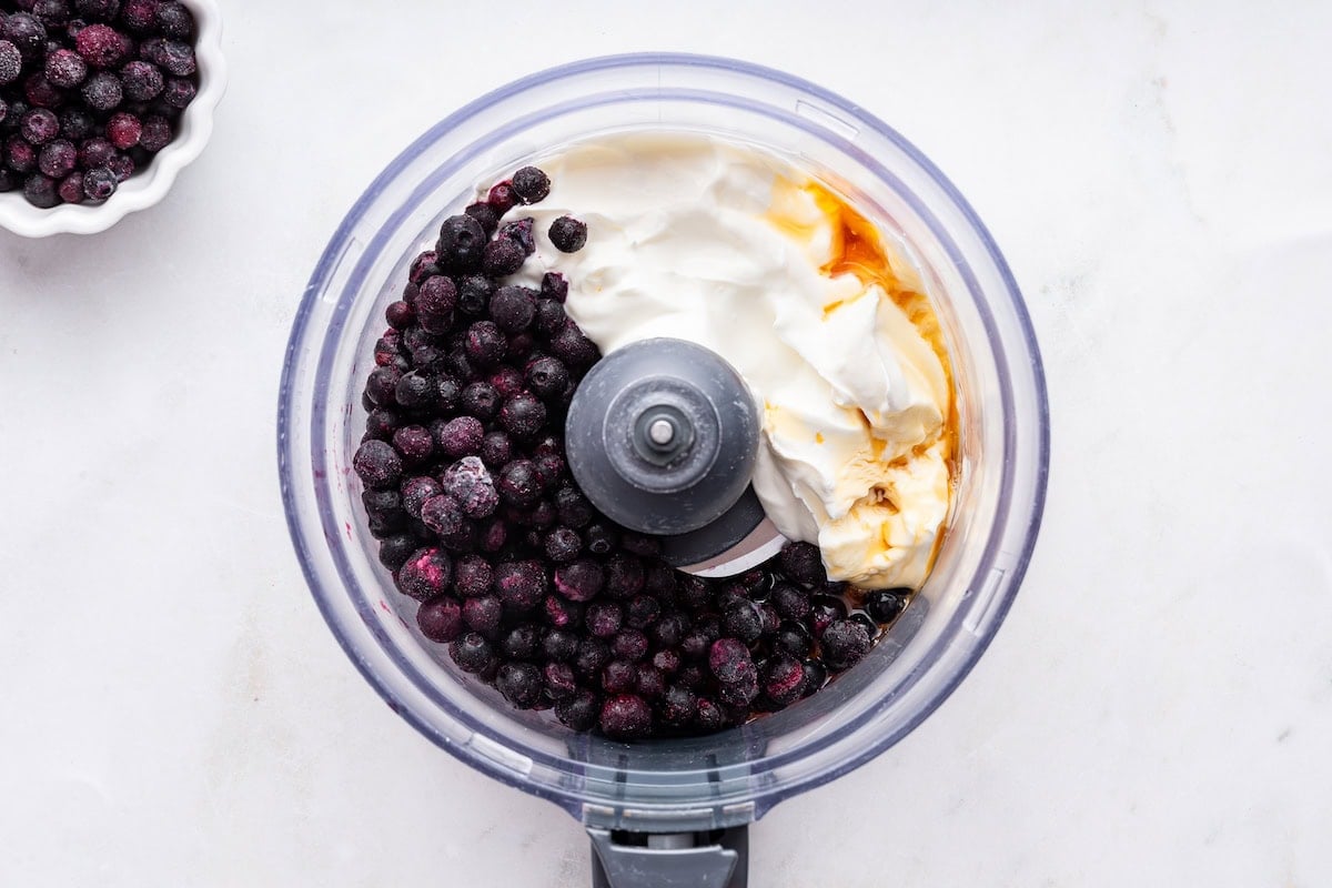 Frozen blueberries, yogurt, and maple syrup in a food processor.
