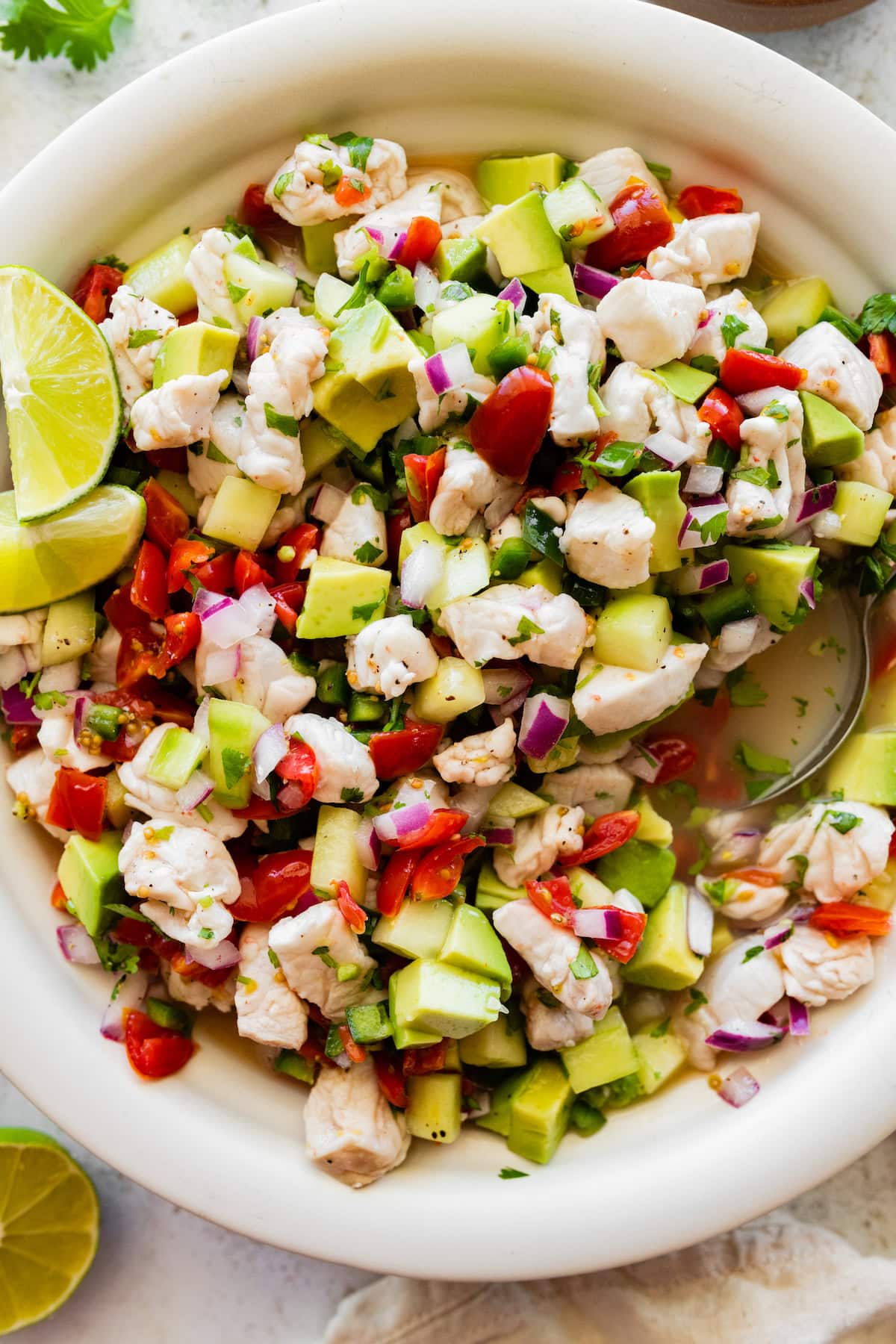 A large white bowl of ceviche with fresh fish, avocado, tomato, cucumber, and avocado.