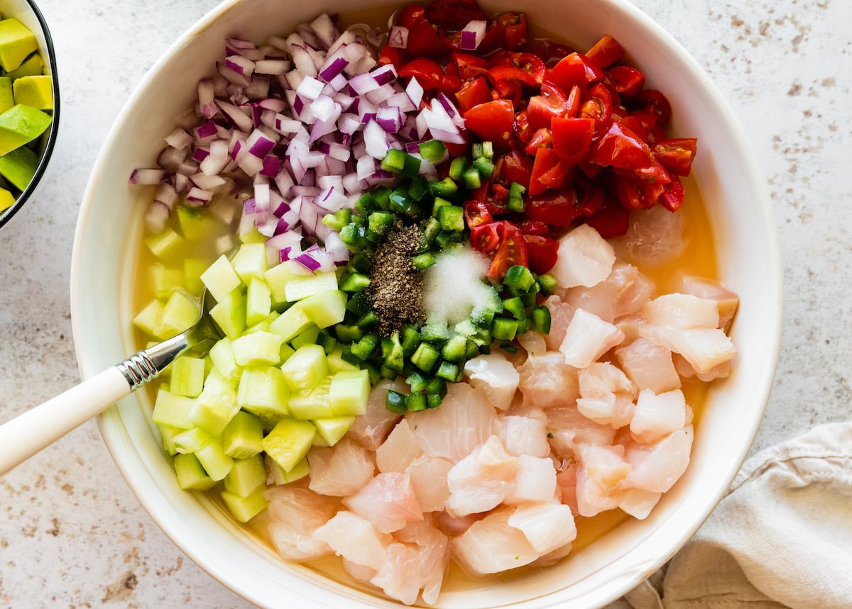 A large white bowl of raw fish, jalapeno, tomato, red onion, and cucumber.