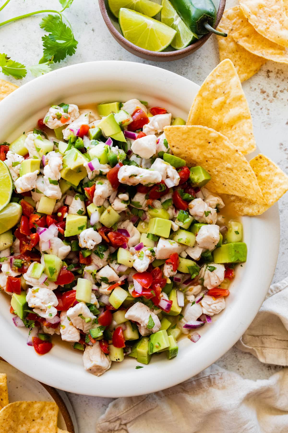 A large white bowl of ceviche with fresh fish, avocado, tomato, cucumber, avocado, and three tortilla chips on the side.