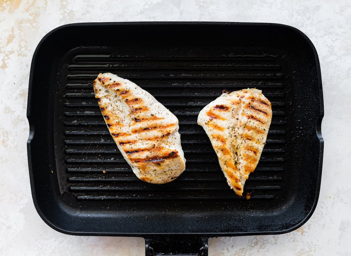 Two grilled chicken breasts in a pan.