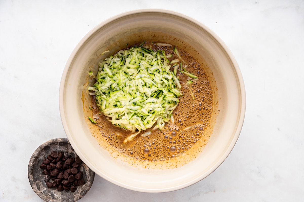 Grated zucchini added to the wet ingredients in a large bowl.