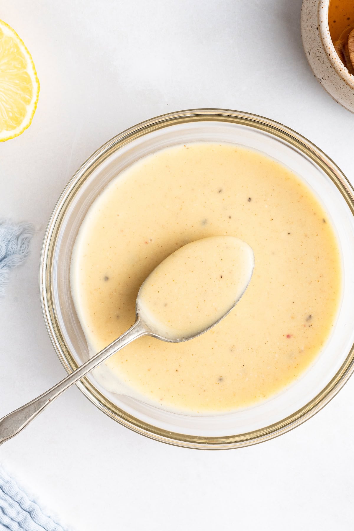 A creamy honey mustard dressing in a small glass bowl with a metal spoon inside.