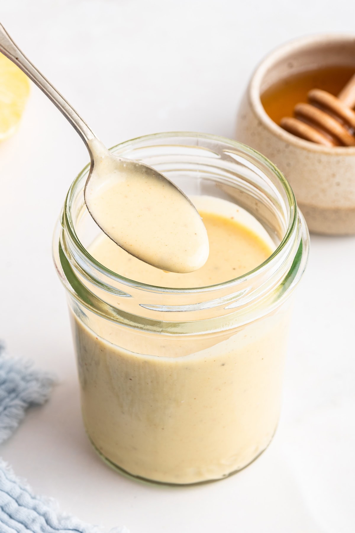 A metal spoon holding a small portion of honey mustard dressing over a mason jar of the dressing.