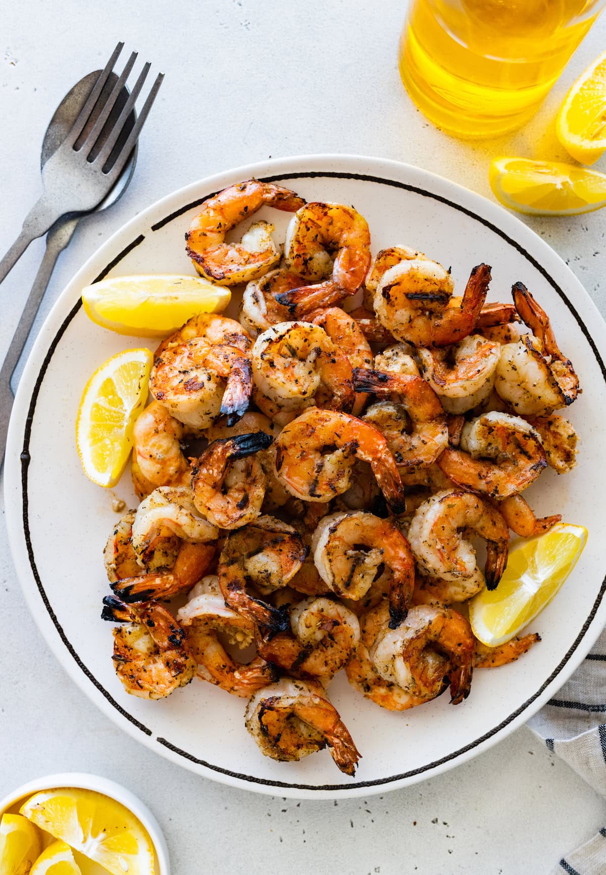 A large plate full of grilled shrimp with lemon wedges on the side.