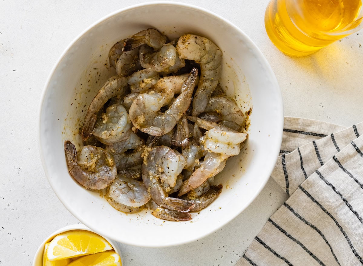 Raw shrimp in a medium bowl with seasoning.