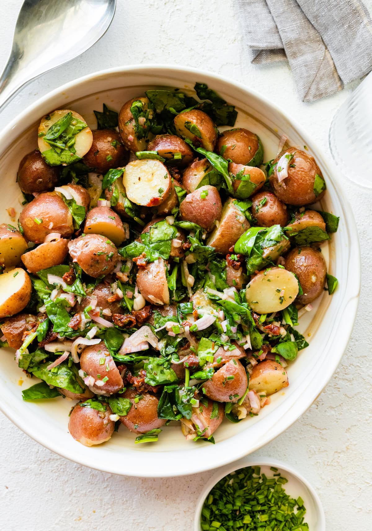 A no mayo potato salad in a large bowl with potatoes, spinach, sun dried tomatoes and fresh herbs.