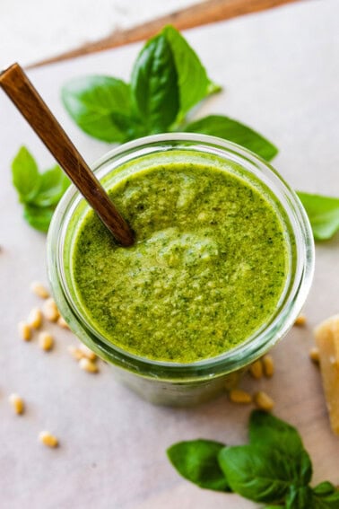 Overhead photo of a glass jar full of homemade pesto with a spoon in the jar.
