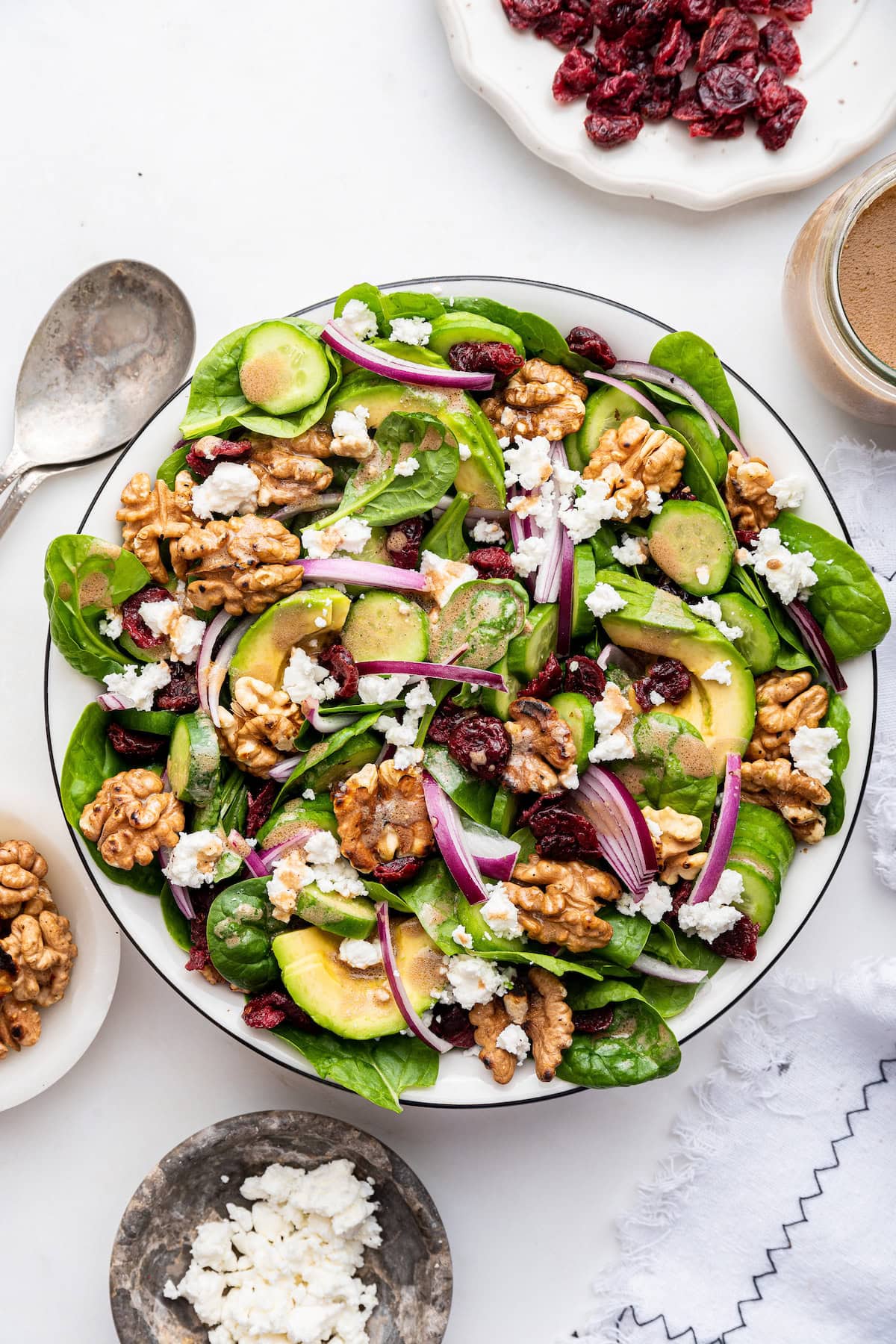A bowl of spinach salad with ingredients like red onion, walnut, avocado, and cranberries.