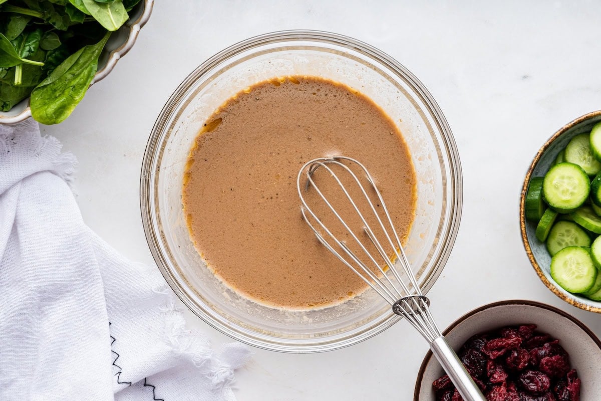 A balsamic dressing in a glass bowl with a metal whisk.