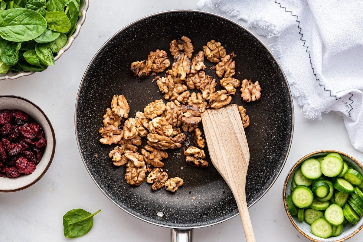 Toasted walnuts in a pan with a wooden spatula.
