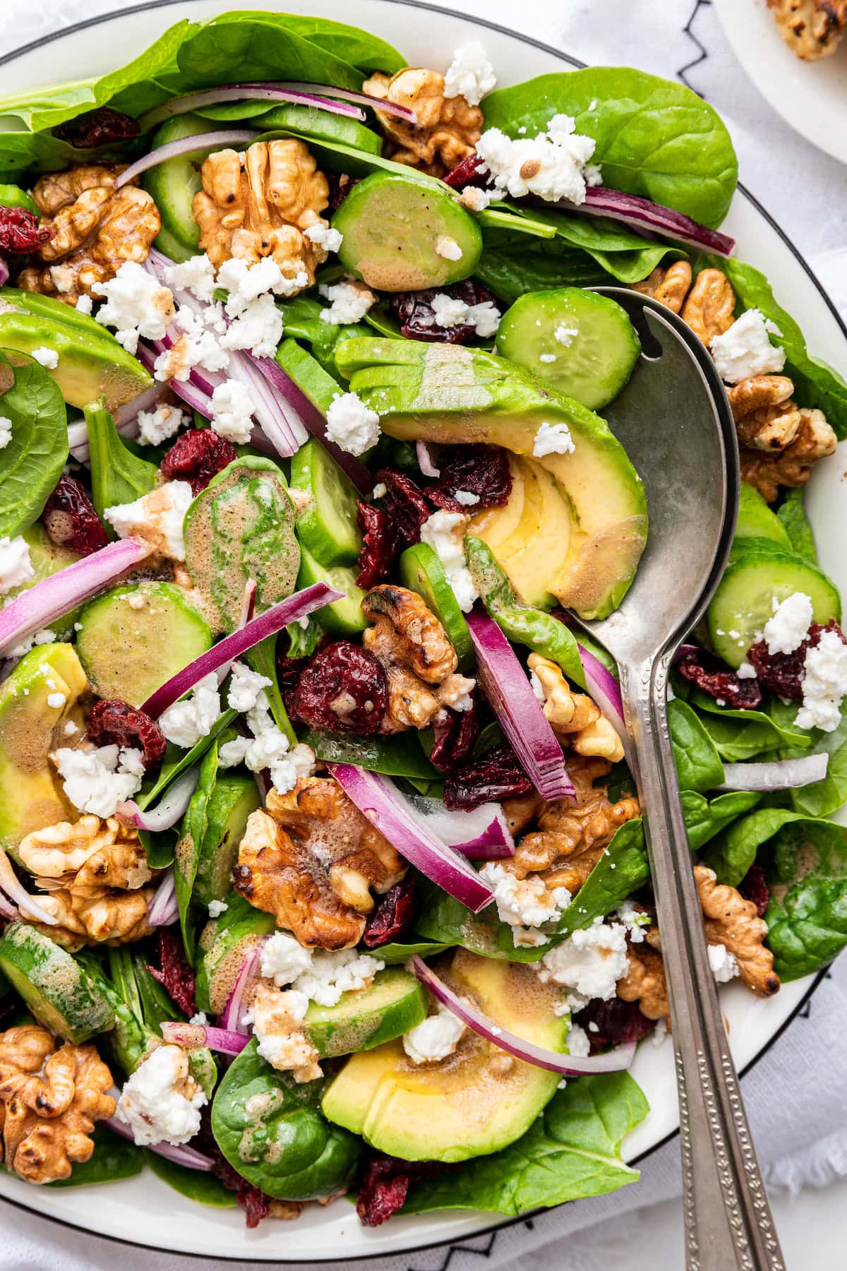 A bowl of spinach salad with ingredients like red onion, walnut, avocado, and cranberries.