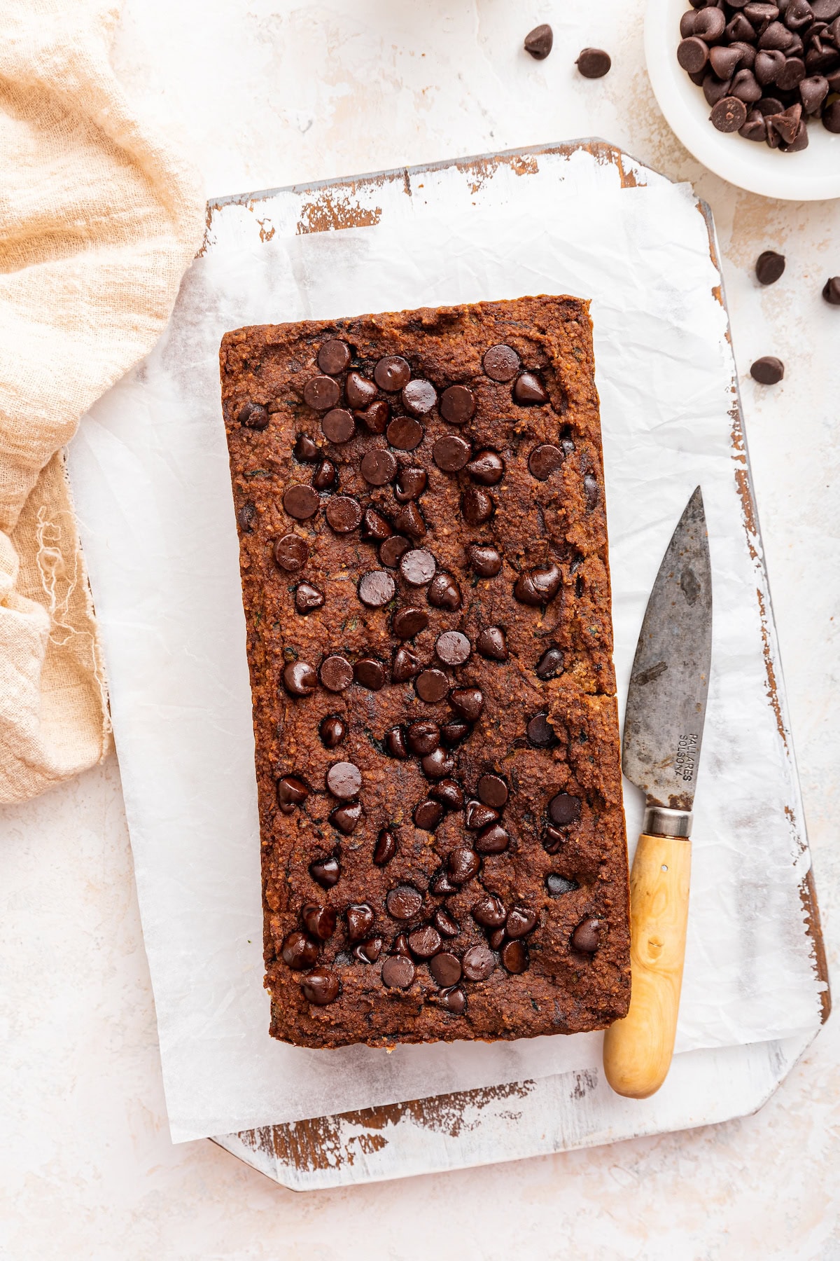 A loaf of vegan zucchini bread topped with chocolate chips on a cutting board.