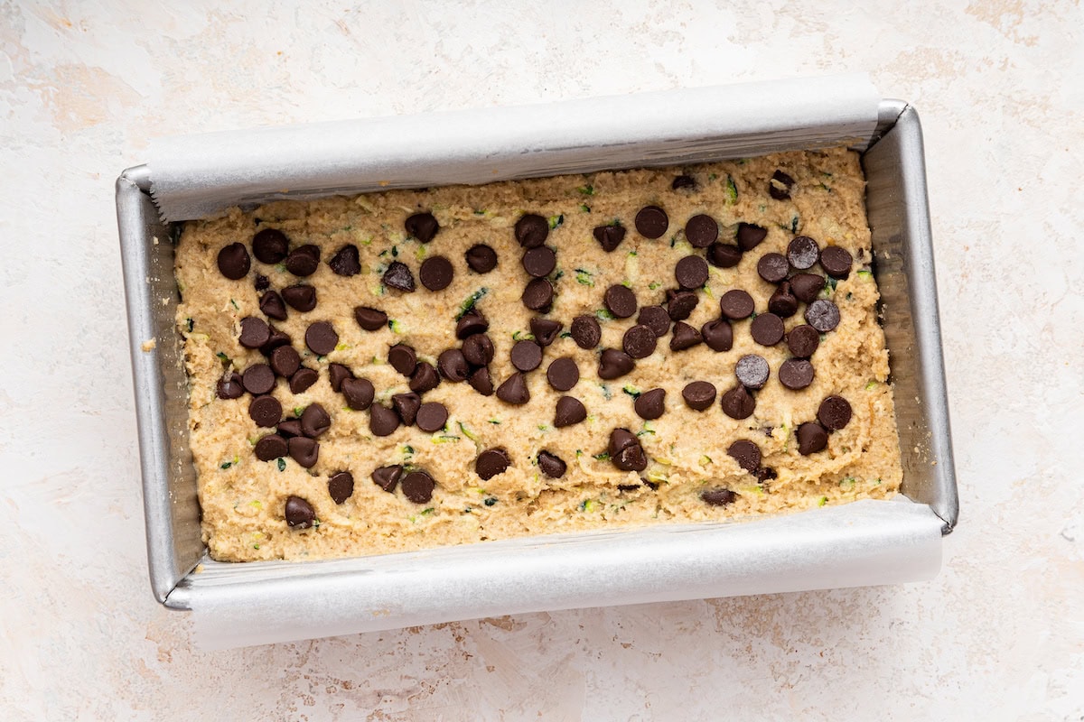 Vegan zucchini bread topped with chocolate chips in a bread pan before being baked.