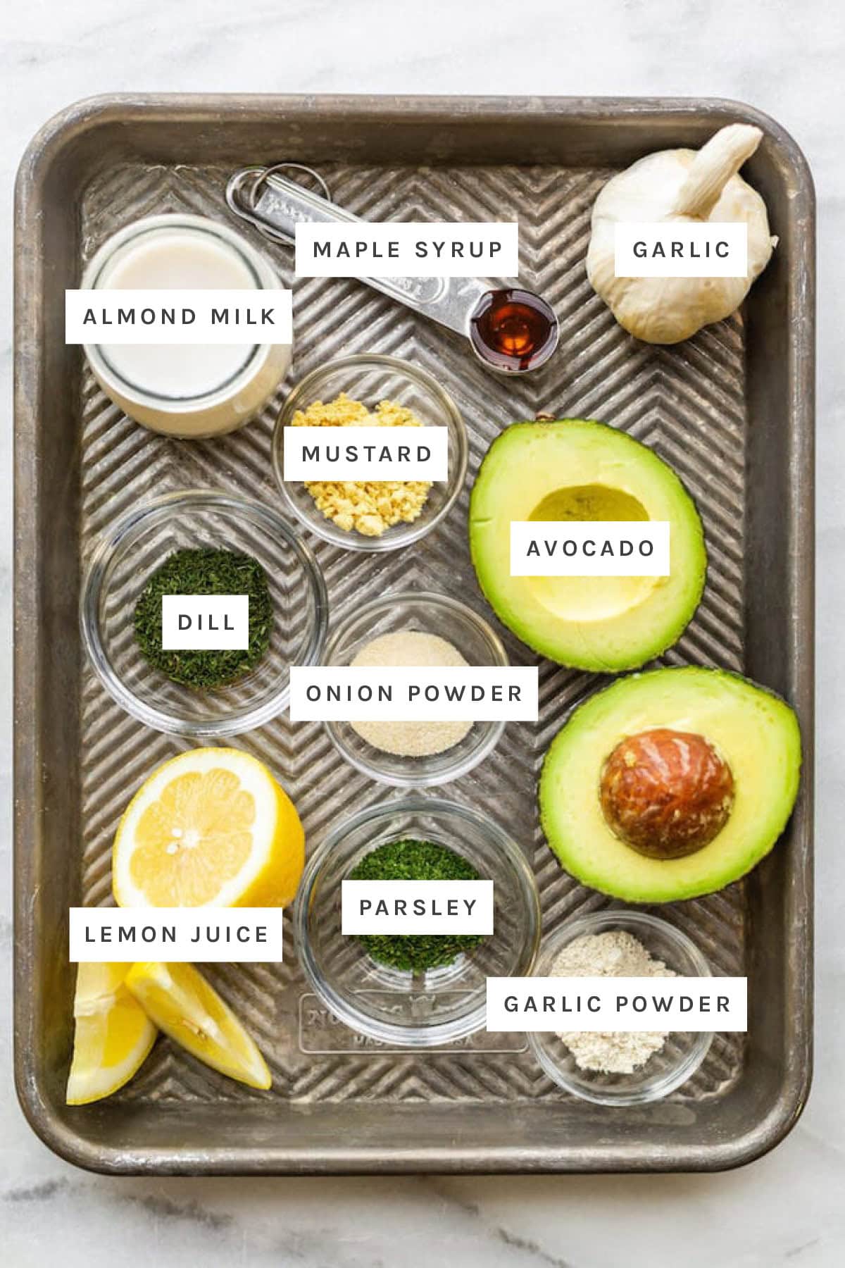 Ingredients measured out to make Avocado Ranch Dressing: almond milk, maple syrup, garlic, mustard, avocado, dill, onion powder, lemon juice, parsley and garlic powder.