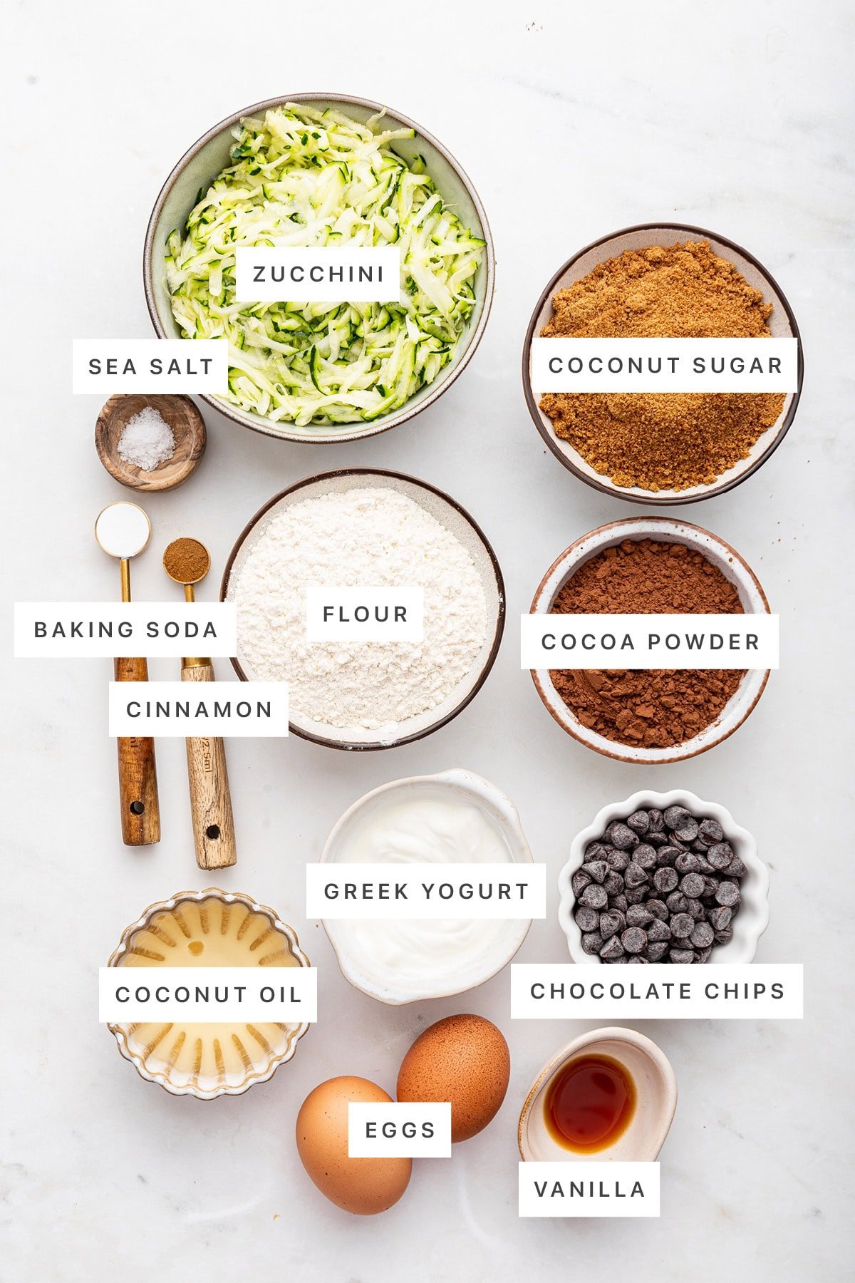Ingredients measured out to make Chocolate Zucchini Bread: zucchini, sea salt, coconut sugar, baking soda, cinnamon, flour, cocoa powder, Greek yogurt, coconut oil, chocolate chips, eggs and vanilla.