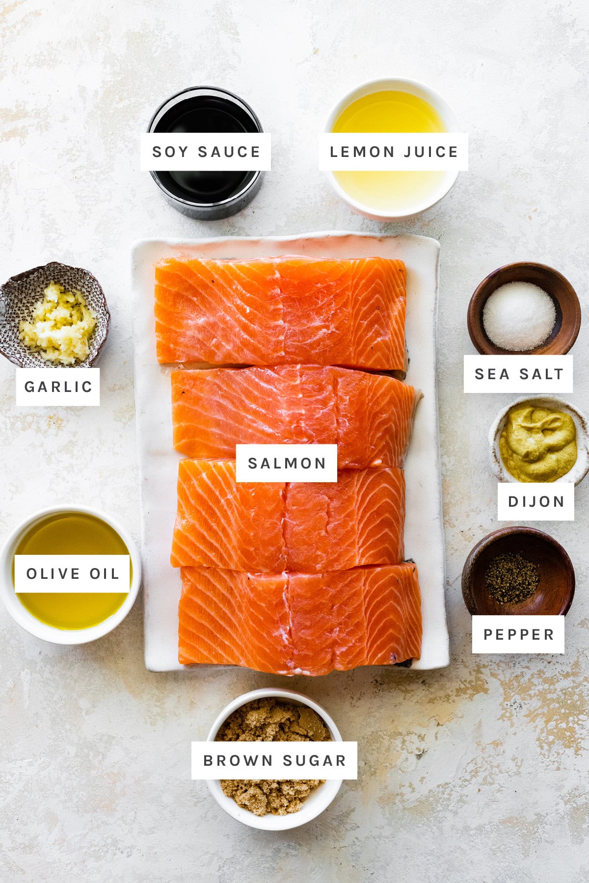 Ingredients measured out to make Grilled Salmon: soy sauce, lemon juice, garlic, salmon, sea salt, dijon, pepper, olive oil and brown sugar.