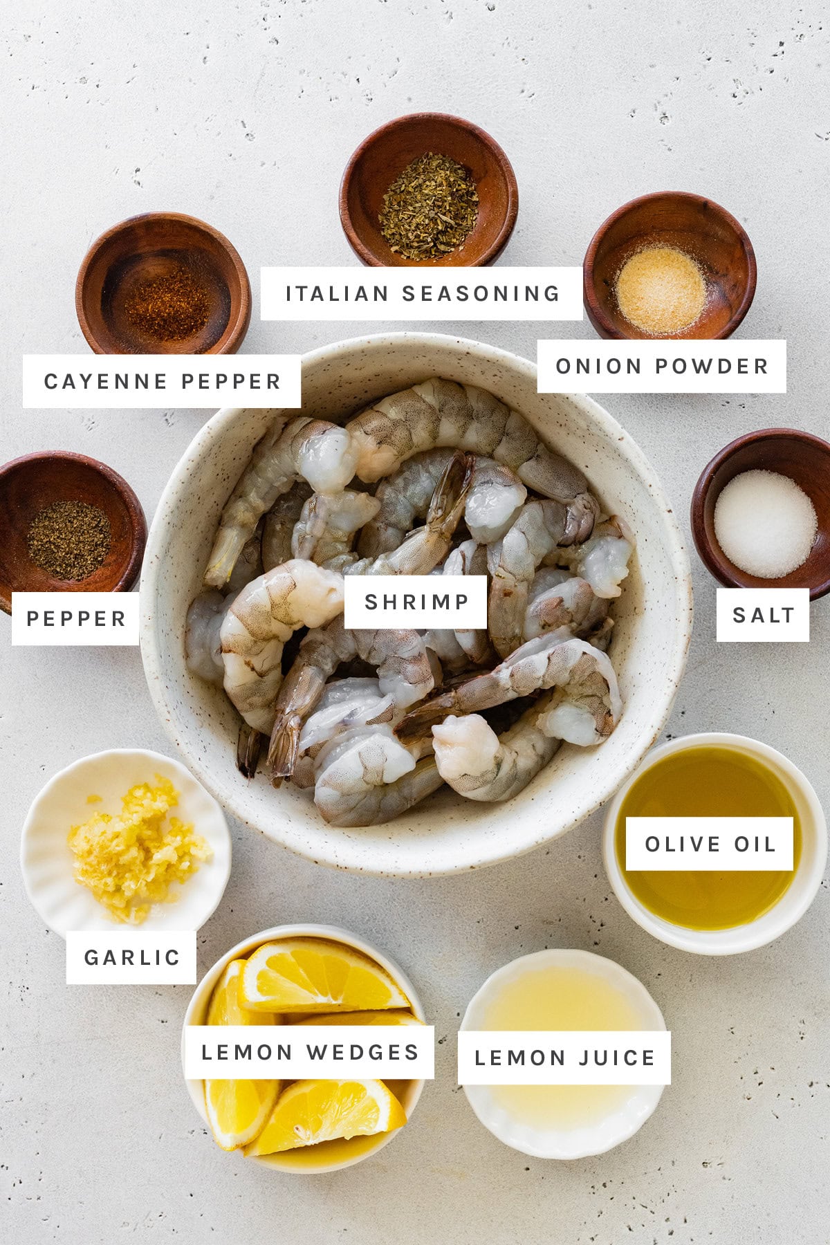 Ingredients measured out to make grilled shrimp: salt, pepper, cayenne pepper, lemon, onion powder, Italian seasoning, shrimp, garlic and olive oil.