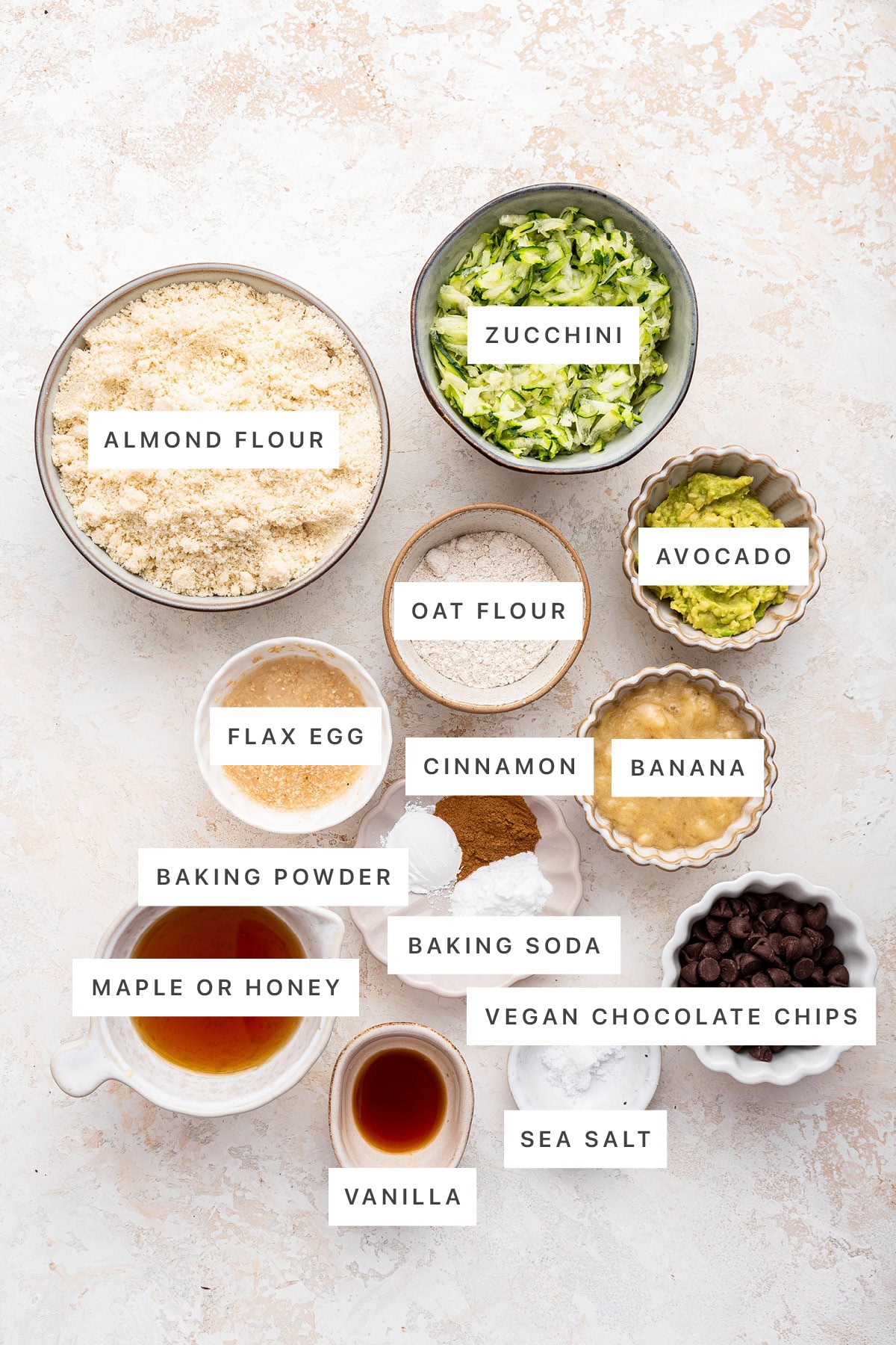 Ingredients measured out to make vegan zucchini bread: almond flour, zucchini, oat flour, avocado, flax egg, cinnamon, banana, baking powder, baking soda, maple syrup, vanilla, sea salt and vegan chocolate chips.