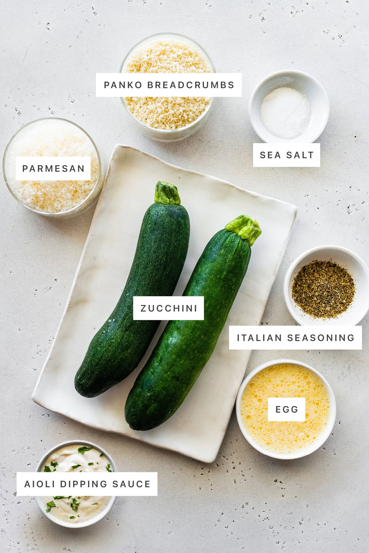 Ingredients measured out to make Crispy Baked Zucchini Fries: panko, sea salt, parmesan, zucchini, Italian seasoning, egg and aioli dipping sauce.