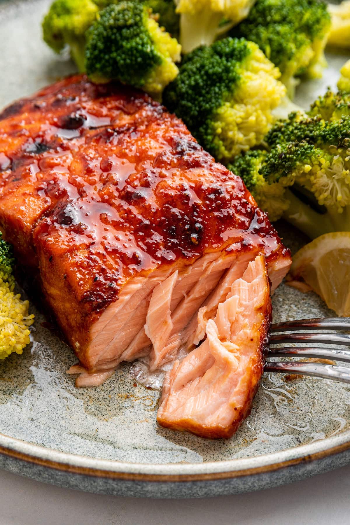 A date glazed salmon on a plate with a fork taking a small portion from the salmon.