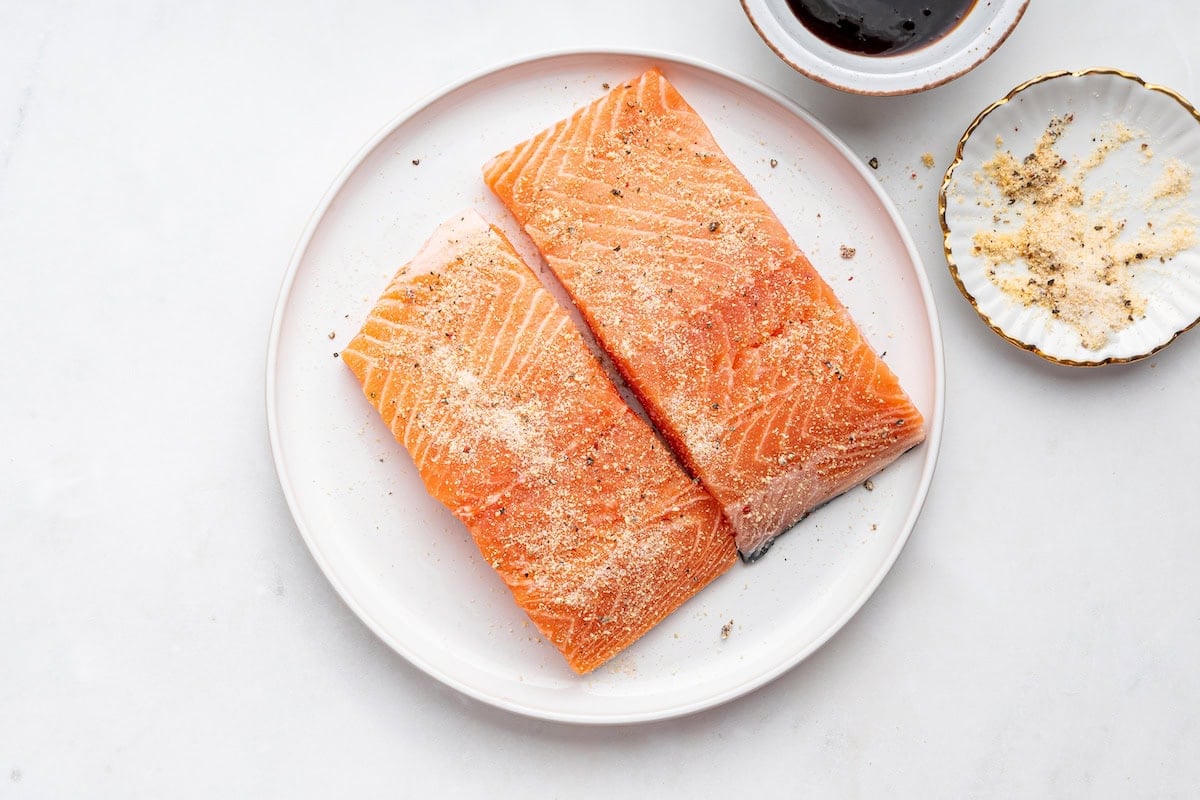 Two raw salmon filets with onion powder, garlic powder, salt, and pepper added to them.