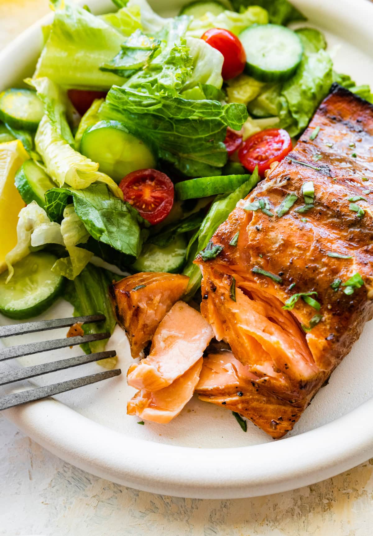 A grilled salmon filet with a fork taking a portion from it on a plate with a side salad.